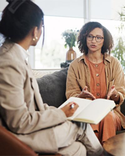 Two people sitting on a couch talking to a professional with a notebook